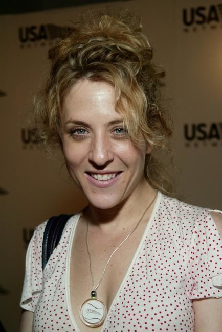 Bitty Schram smiling with messy hair while wearing a white and red polka dot blouse and necklace