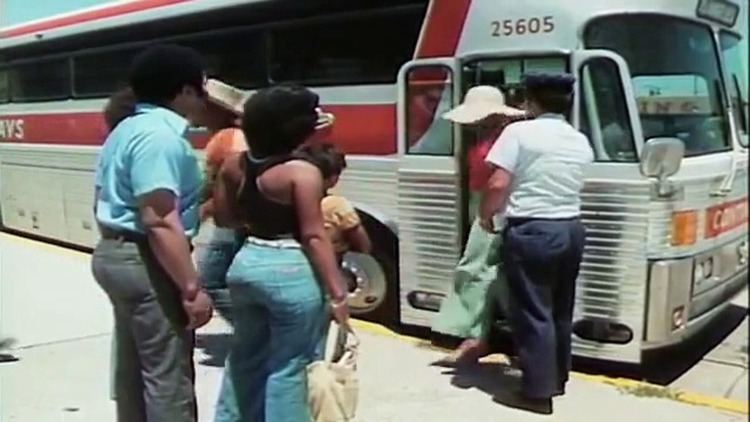 A group of black people waiting to enter the red and white bus in a scene from the 1974 Blaxploitation film written and directed by Jamaa Fanaka, Black Sister's Revenge.