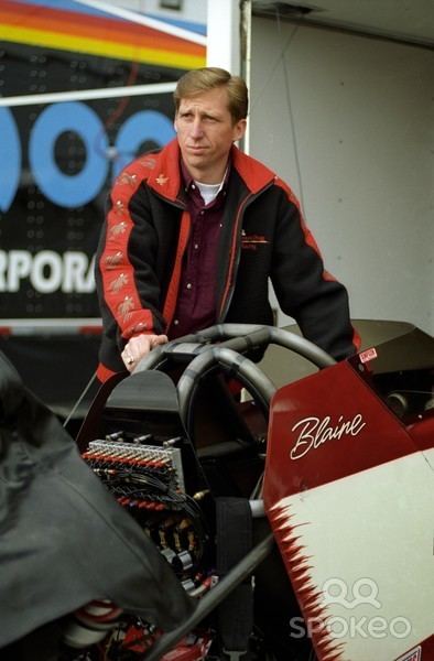Blaine Johnson standing beside his red racing car wearing a maroon shirt over a red jacket