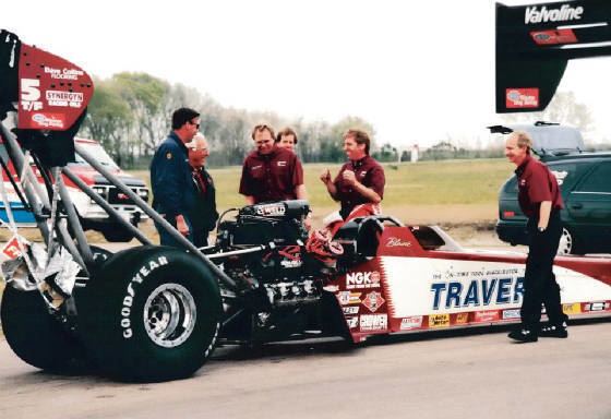 Blaine Johnson standing beside his racing car doing gestures while talking with his lifelong crew chief and wearing a red shirt