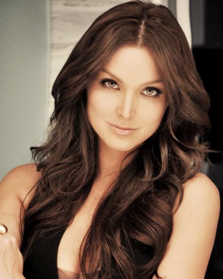 Blanca Soto smiling with her wavy hair down and wearing a black blouse exposing her cleavage