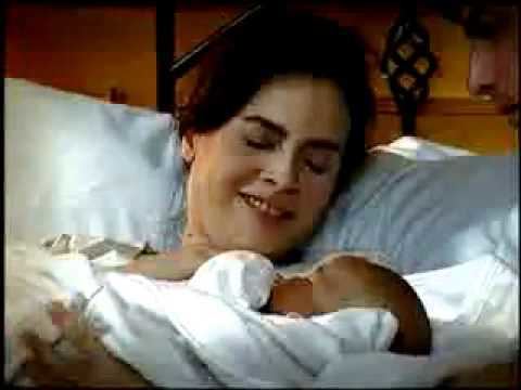 The movie scene of Blusang Itim (2011), Rita Avila is smiling, laying on the bed while holding a newborn baby in white cloth, has black hair wearing a white clothes, at the right is a man looking at the newborn.