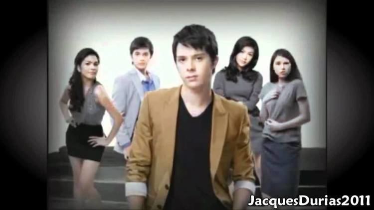 The movie scene of Blusang Itim (2011), at the back, from left, a woman is smiling standing, posing with his left hand on the hips and right hand on the waist  has long black hair wearing a gray sleeveless top and a black skirt, 2nd from left, a man is serious, standing, has black hair wearing a blue polo under a silver coat, 3rd from left, a woman is serious, standing arms crossed, has black hair wearing a gray long sleeve dress, at the right, a woman is serious, standing, has long black hair wearing a gray uniform and gray skirt, in front, Frank Magalona is serious, standing, has black hair wearing a black shirt under a brown coat, at the bottom right is word “JacquesDurias2011”