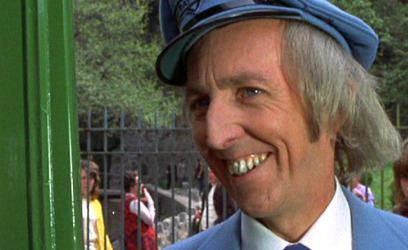 Bob Grant smiling while looking at something while wearing a blue peaked cap and white long sleeve under a blue coat