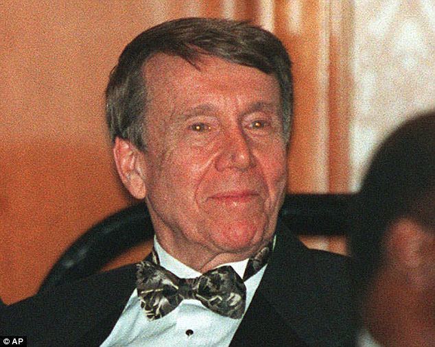 Bob Grant with a tight-lipped smile while looking afar and wearing a white long sleeve under a black and gray bow tie and black coat