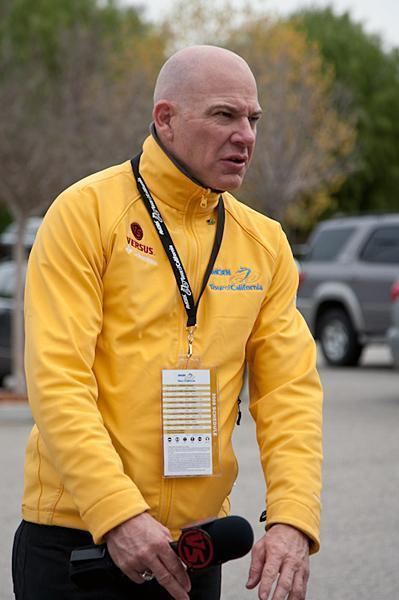 Bob Roll holding a microphone and wearing a yellow jacket and black pants