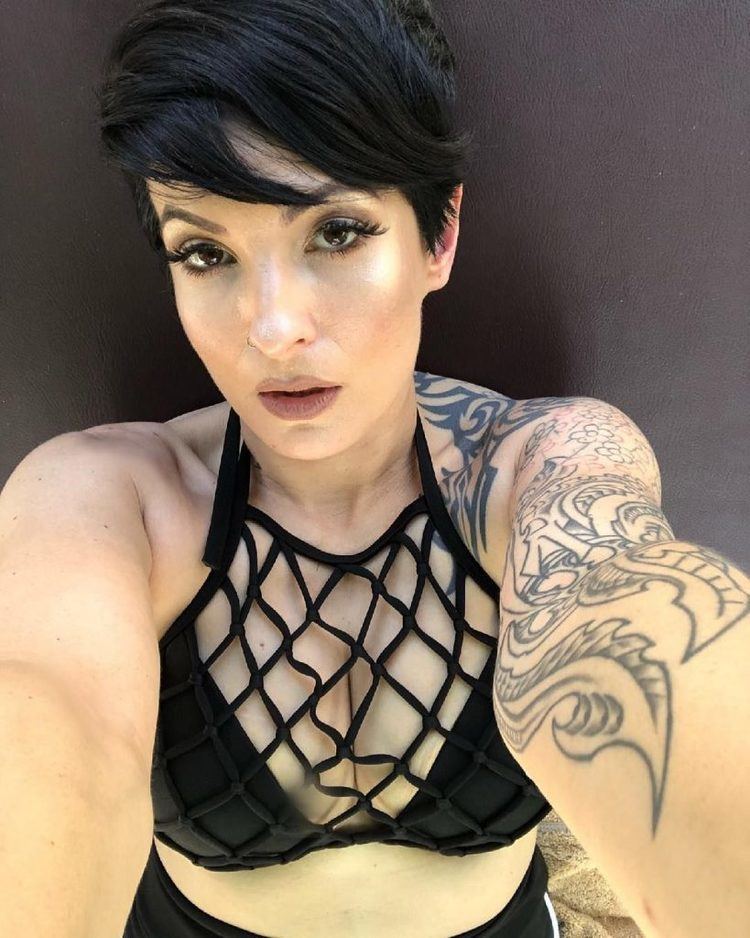 Bobbi Jo Black looking fierce in her short hairstyle with bangs and tattoos on her right arm while wearing a black netted halter bikini