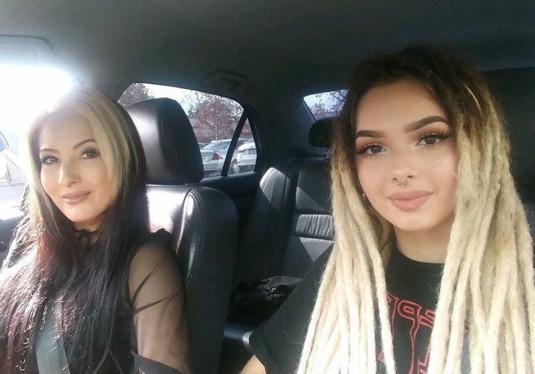 Bobbi Jo Black smiling while wearing a black blouse and seatbelt inside a car with her daughter Zhavia Ward in a blonde hair and black shirt