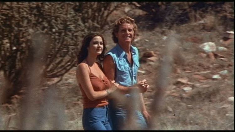 Marjoe Gortner and Lynda Carter smiling while walking hand in hand in a scene from the 1976 crime drama film, Bobbie Jo and the Outlaw