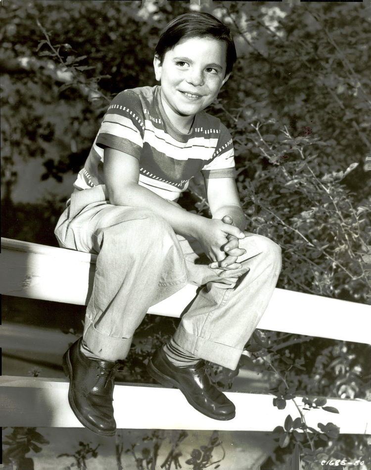 Young Bobby Clark sitting on a fence and wearing striped shirt and pants