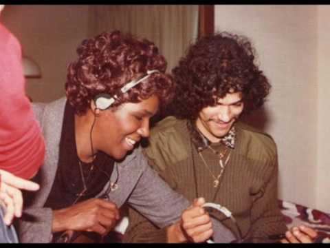 Bobby DeBarge smiling and wearing green long sleeves while the man beside him wearing a headset, gray coat, and black shirt