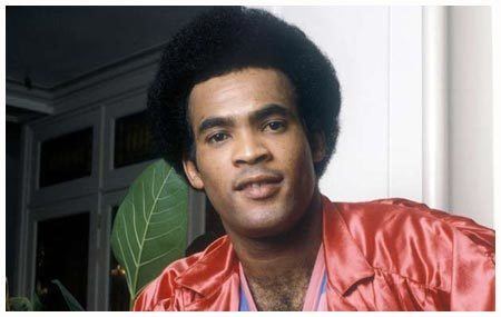 A younger Bobby Farrell smiling inside a house and wearing a red leather jacket.