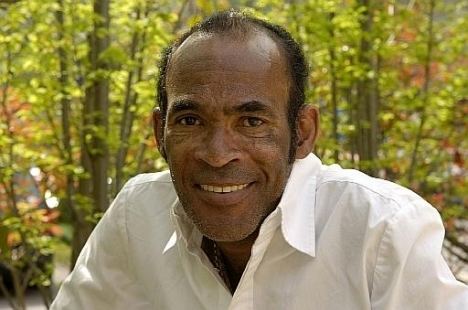 Bobby Farrell smiling with shorter hair and wearing a white long-sleeved polo shirt.