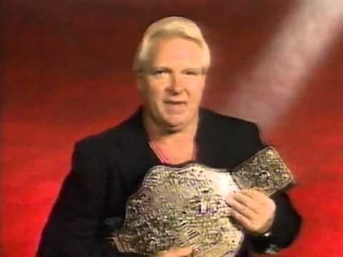 Bobby Heenan smiling while holding the championship belt and wearing a black coat