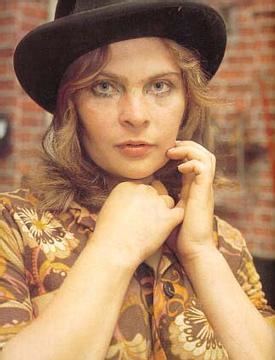 Bodil Joensen's hands on her face while wearing a black hat and brown and yellow floral blouse