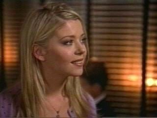 Tara Reid smiling, with blonde hair, and wearing a purple shirt in a movie scene from Body Shots (1999 film).
