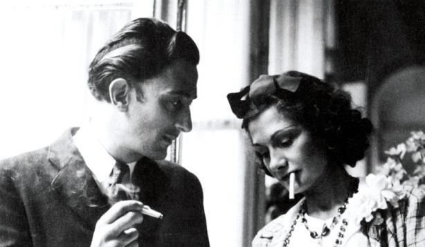 Arthur Edward "Boy" Capel is smoking while looking at Coco Chanel smoking. Boy Capel wearing a black coat while Coco with a ribbon on her head, wearing a necklace, and a white dress.