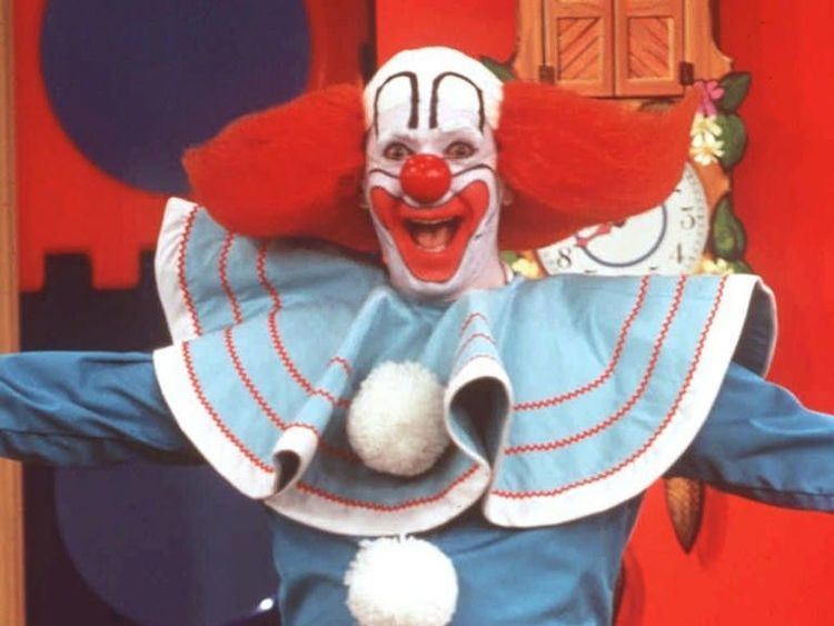 Bozo the Clown smiling with his arms open and wearing a blue, red, and white neck ruffle collar and blue long sleeves