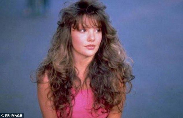 Brandi Brandt, sincerely looking at someone from a scene in an episode of the television sitcom "Desperately Seeking Miss October", has brown curly hair and wearing a pink sleeveless top.