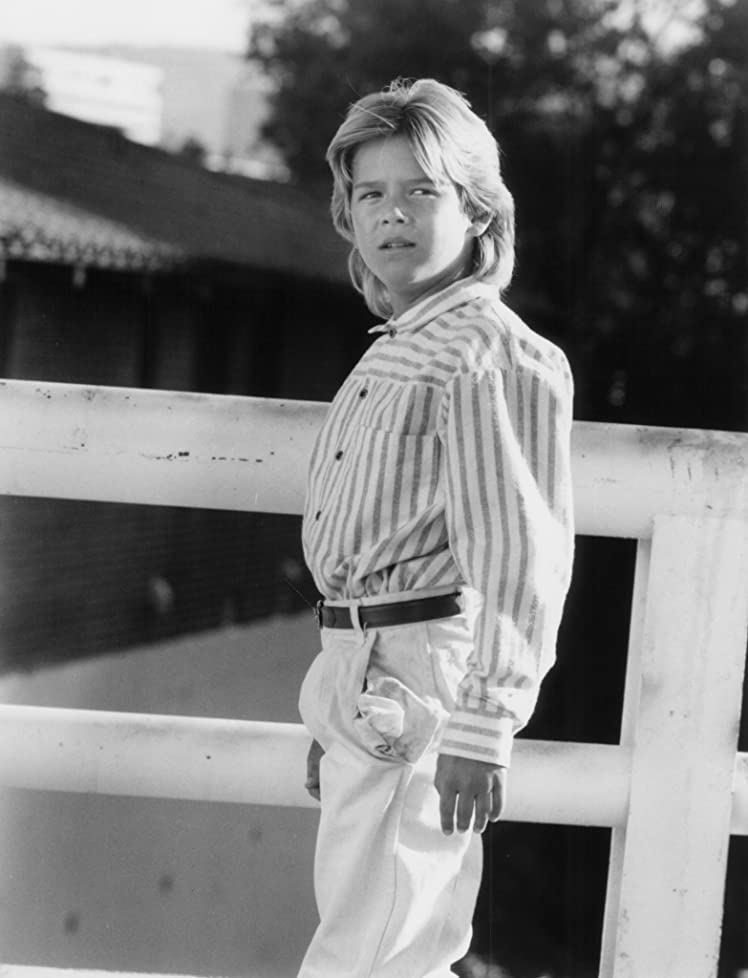 Brandon Call at a young age, with blonde hair and wearing striped long sleeves and white pants.
