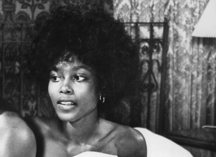 Brenda Sykes in a movie scene laying in a bed with thick bushy hair.