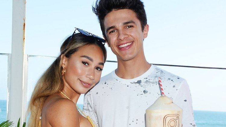 Eva Gutowski smiling together with Brent Rivera at the beach, holding a drink and wearing a white and black shirt