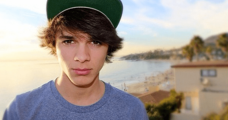 Brent Rivera looking serious and wearing a blue round neck shirt and a green cap