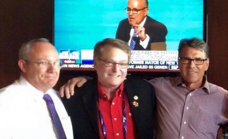 Brian Birdwell smiling with two gentlemen on his side. Brian wearing eyeglasses and a black coat over red long sleeves.