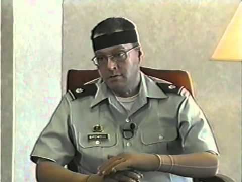 Brian Birdwell with a serious face while sitting on a chair, wearing a black headband, eyeglasses, and a light green polo shirt uniform.