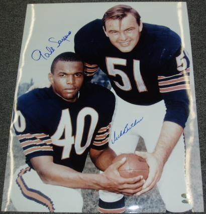Gale Sayers and Dick Butkus smiling and holding a ball together while wearing their football jersey in a poster with their signature