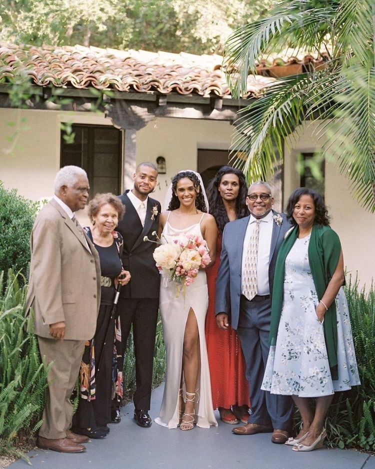 Kris Bowers, Briana Henry, and their family smiling together during the wedding ceremony while Briana wearing a veil and wedding dress with slits