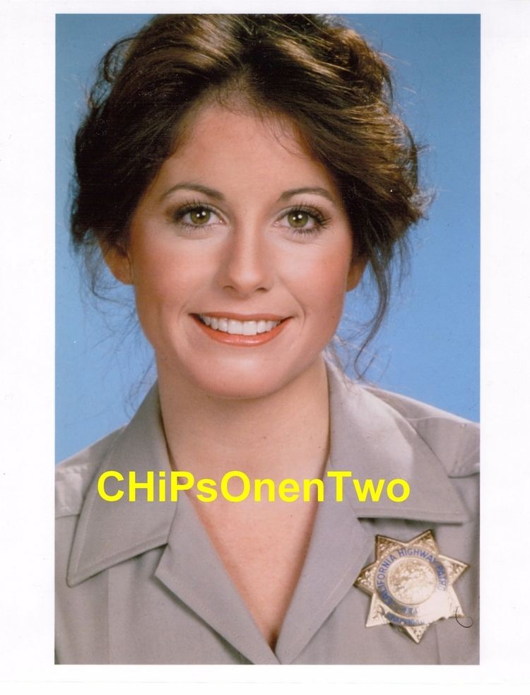 On a Chips film is a picture of Brianne Leary smiling, has brown wavy hair, wearing a gray police uniform with a police badge on her left chest.