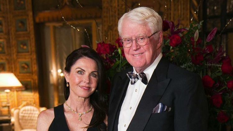 Bridget Rooney smiling in a black dress together with her current husband, Bill Koch in a black suit