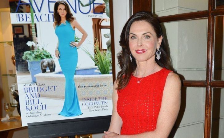 Bridget Rooney smiling and sitting beside a poster featuring herself while wearing a red knitted dress and dangling earrings