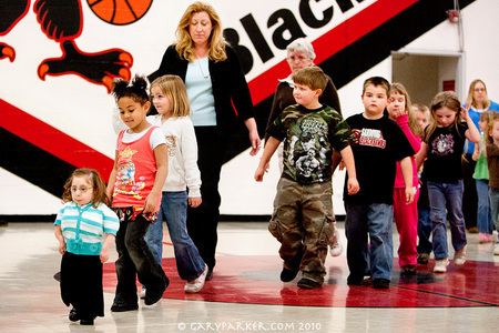 Bridgette Jordan is in the front together with other children lining up. Bridgette is wearing eyeglasses, a white and blue top and black pants