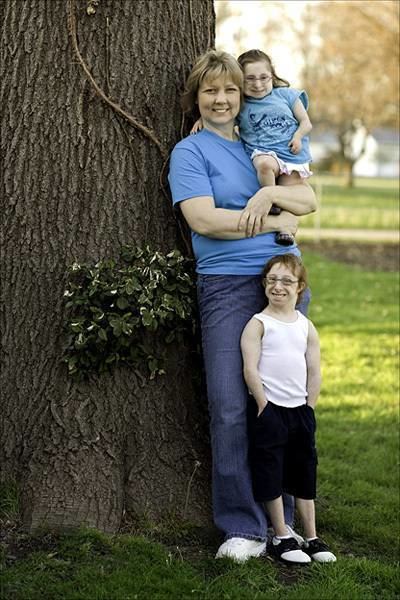 Bridgette and Brad Jordan with their mom Christy Jordan are smiling. Bridgette is wearing eyeglasses, a blue shirt, and white shorts, Brad is wearing eyeglasses, white sleeveless, and black shorts paired with black and white shoes while Christy is wearing a blue shirt, and blue jeans, and white shoes.