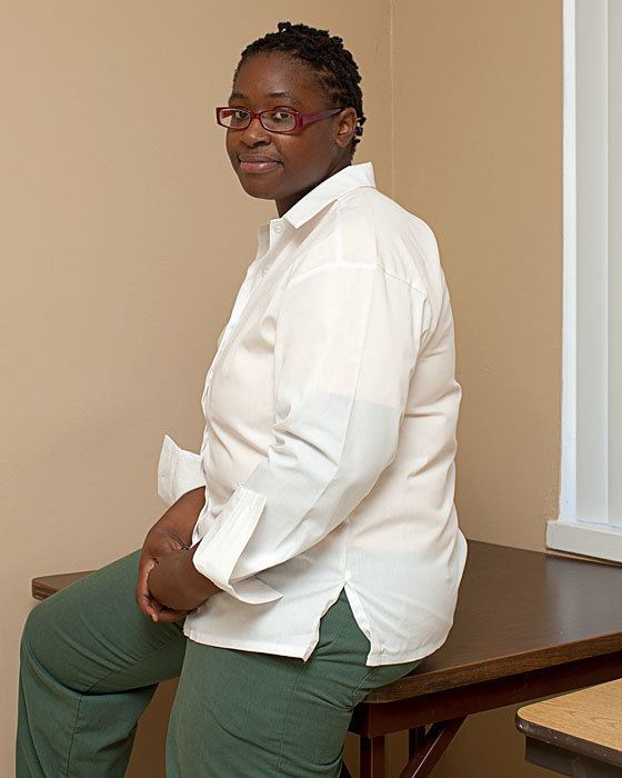 Brigitte Harris sitting on a table wearing a white polo shirt, gray pants, and a pair of eyeglasses
