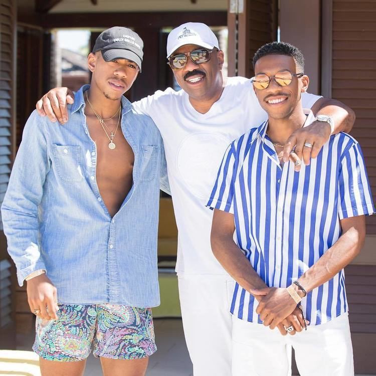 Wynton Harvey, Steve Harvey, and Broderick Harvey Jr are smiling together while Steve holding a cigarette and wearing a white t-shirt