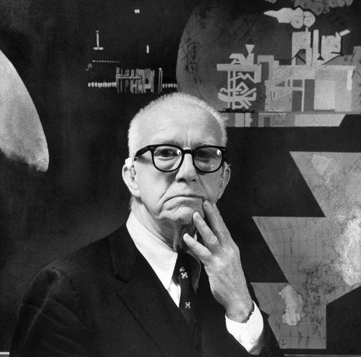 Buckminster Fuller's hand on his face while wearing eyeglasses, coat, long sleeves, and necktie