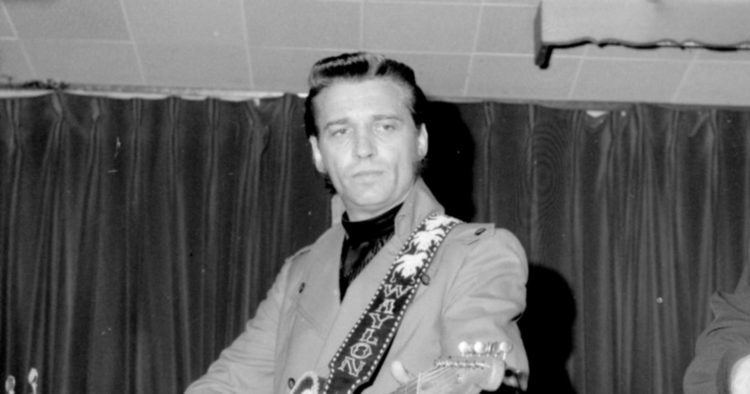 Waylon Jennings playing guitar while wearing a coat and long sleeve