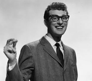 Buddy Holly with a big smile while snapping his finger and wearing eyeglasses, striped coat, long sleeve, and necktie