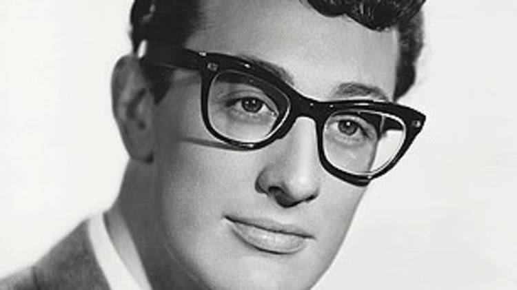 Buddy Holly looking at something while wearing cat eye glasses, coat, long sleeve, and necktie