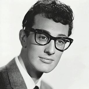 Buddy Holly looking at something while wearing cat eye glasses, coat, long sleeve, and necktie