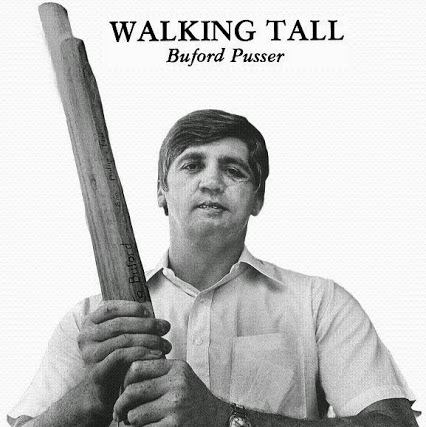 Buford Pusser is serious, has black hair, both hands holding a wood, above him is the title “WALKING TALL” and his name “Buford Pusser” he is wearing a wristwatch on his left hand and a white polo.