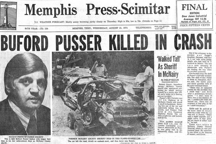 In a newspaper, the headline “BUFORD PUSSER IS KILLED IN CRASH”. Buford Pusser (left) is being serious, has black hair, wears white long sleeves with black lines, and a black necktie under a black suit. In the middle is a crashed car with two men checking on the situation. On right is a news report saying “Walked Tall” As Sheriff In McNairy.
