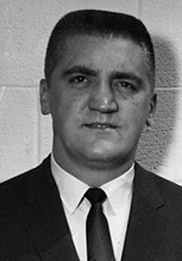 Buford Pusser is serious, has black hair, wears white long sleeves, a black necktie under a black suit.