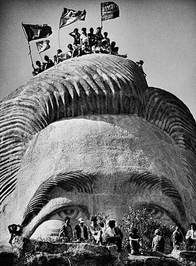A large bust of Ferdinand Marcos carved into a hillside is overtaken by demonstrators