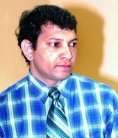 C K Anil wearing a blue checkered shirt and a striped blue tie.