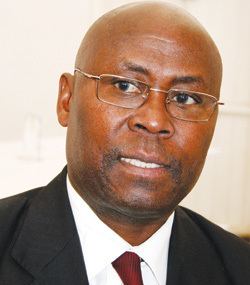 Cain Mathema looking at something while wearing a black coat, white long sleeves, maroon necktie, and eyeglasses