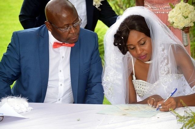 Bathabetsoe Diana Nare Mathema signing on the paper while Cain Mathema looking at it and sitting beside her during their wedding day